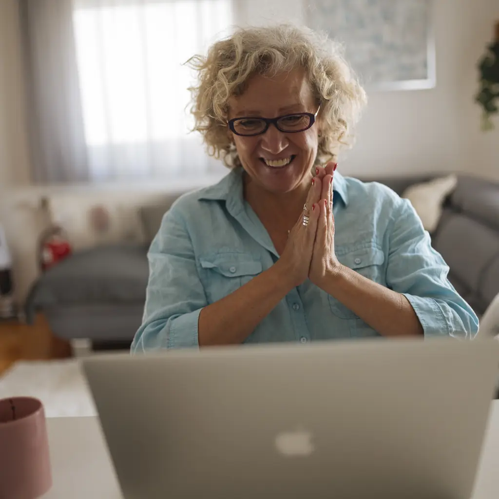 An older woman smiling during a video call on her laptop at home.