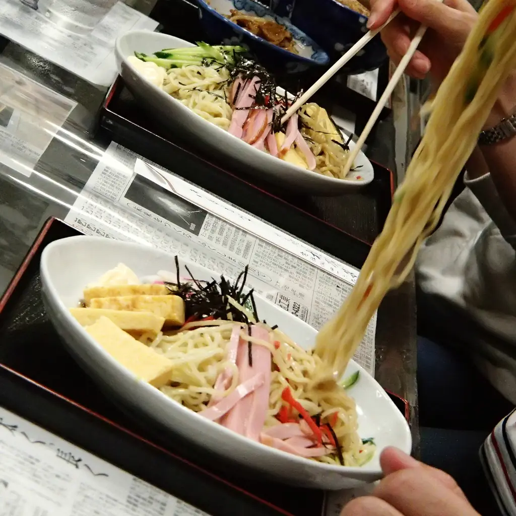 Chopsticks lifting cold noodles from a bowl.