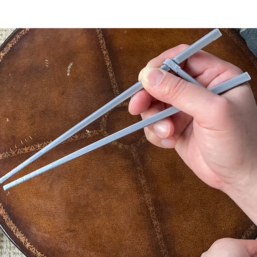 A hand holding training chopsticks in a closed position.